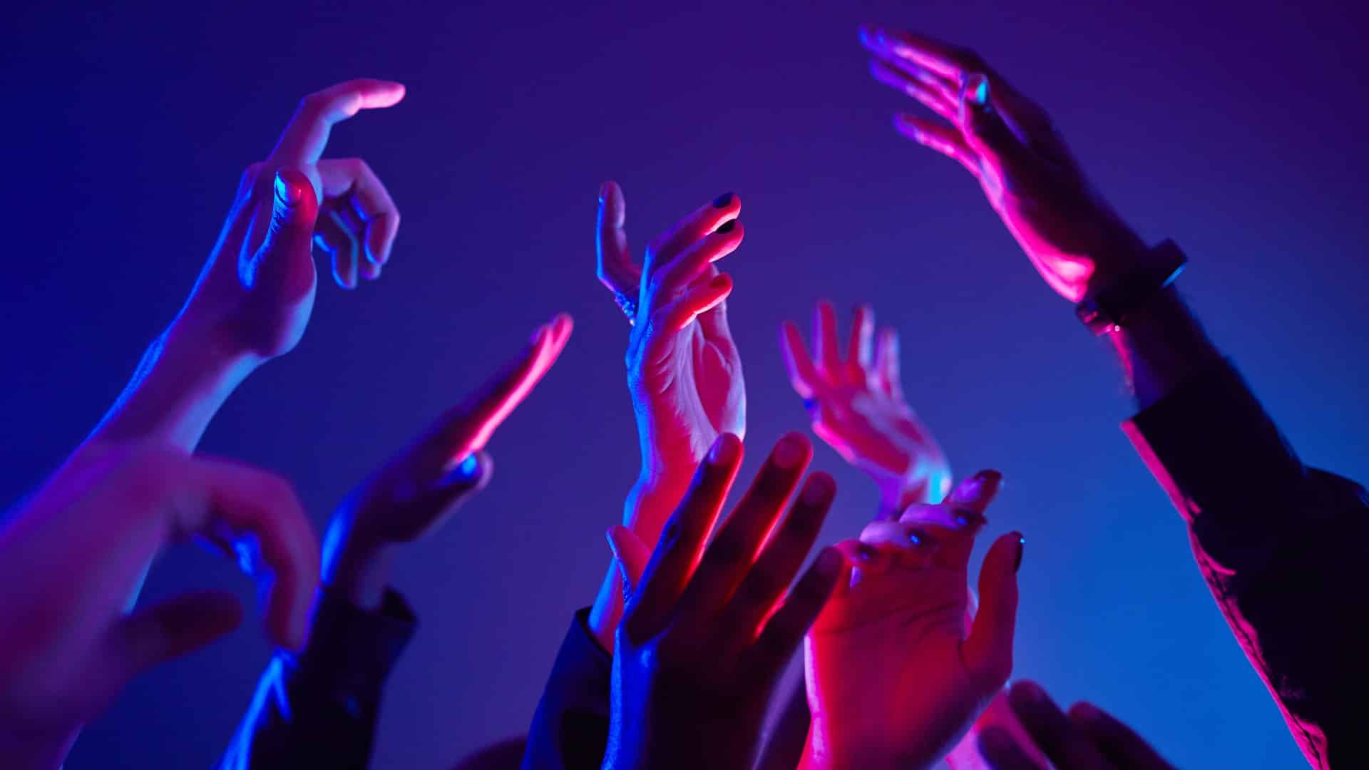 Close up of crowd dancing in club with hands up lit by neon lights, copy space