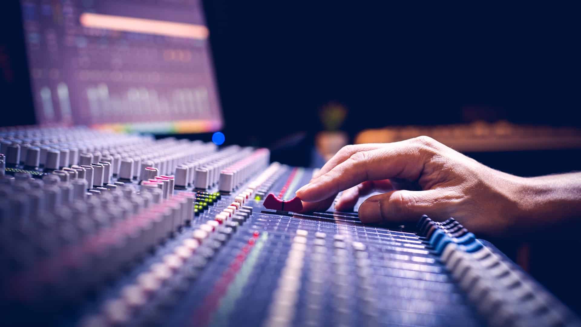 male producer, sound engineer hands working on audio mixing console in broadcasting, recording studio
