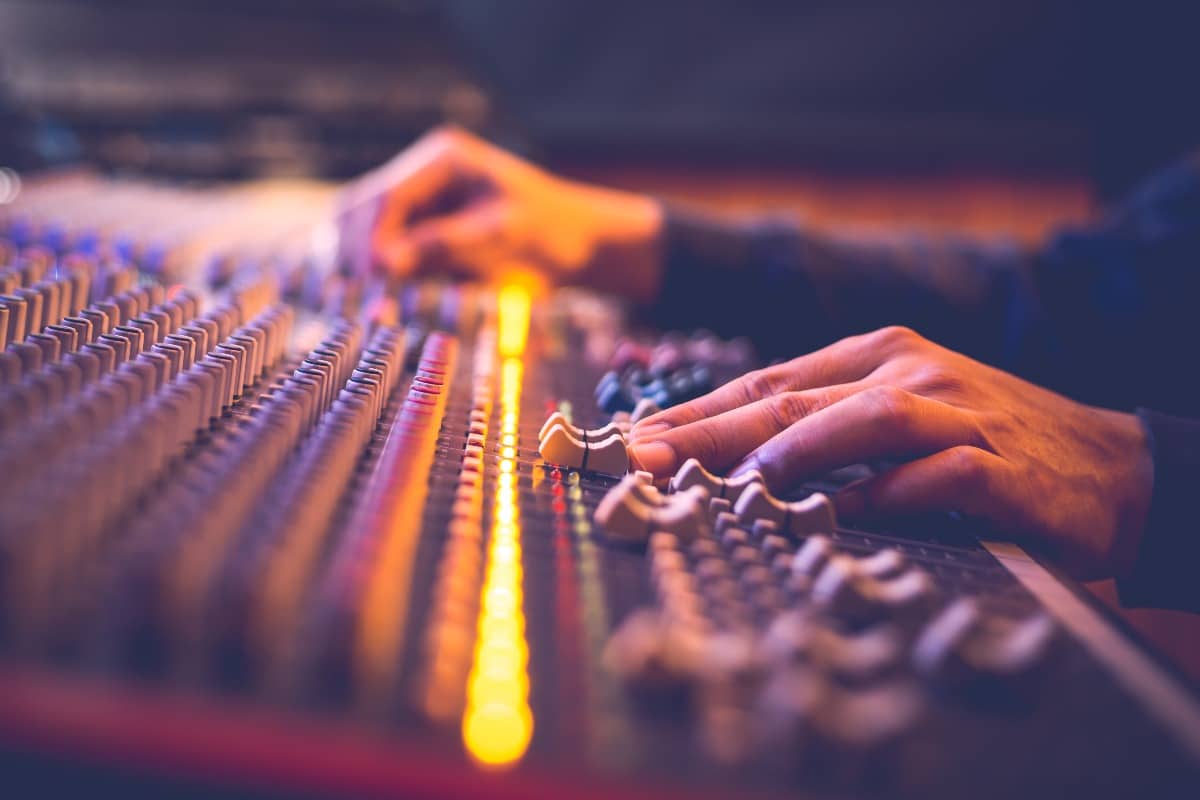 male producer, sound engineer hands working on audio mixing console in broadcasting, recording studio